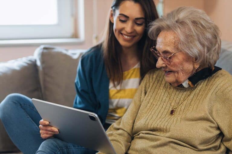 Craft & Communicate | Senior woman smiling as she looks at a tablet held by her caregiver